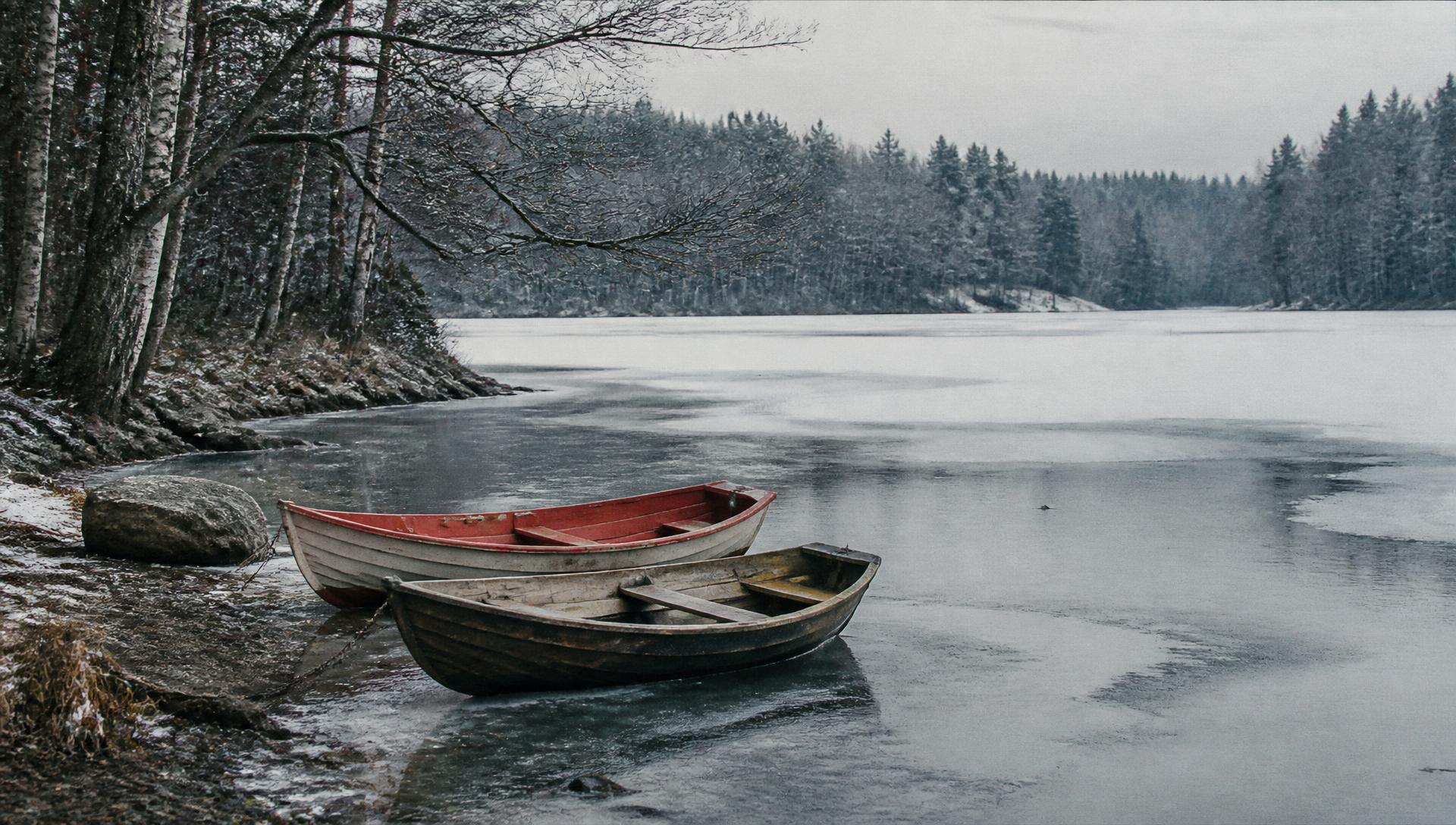 Two small wooden boats resting at the edge of a partially frozen Nordic lake
